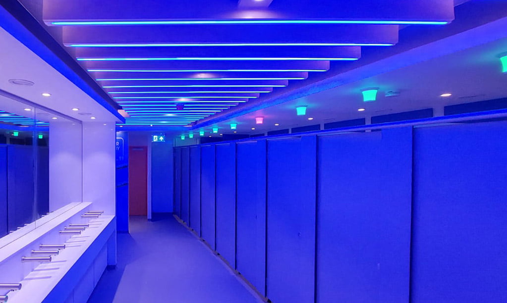 A washroom with blue lighting and blue toilet occupancy sensor lights above each cubicle